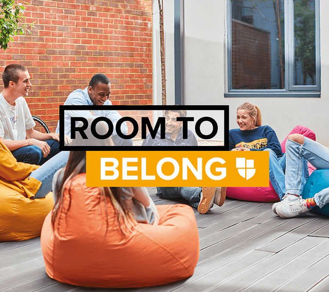 Young adults sit in beanbag chairs, socializing in an outdoor patio area. ROOM TO BELONG is overlaid on the image.