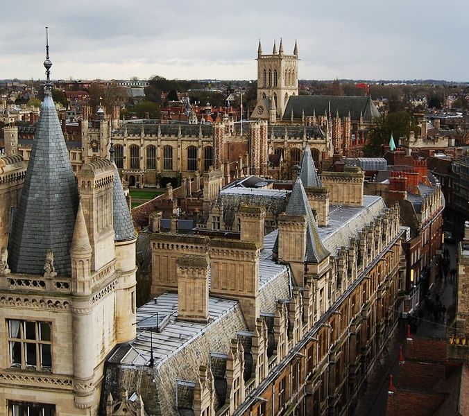 A stone tower overlooks a city. Numerous buildings with steep roofs and spires are densely packed together. The context is a historic European city.