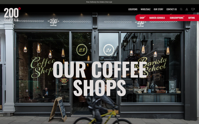 A storefront, displaying "200° Coffee" and "Barista School," is shown with a cyclist passing by. The shop is modern with large windows; the text “OUR COFFEE SHOPS” overlays the image. Free delivery is offered on orders over £30.